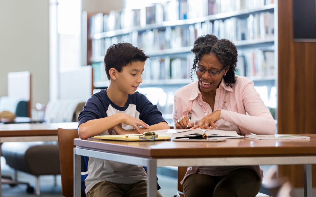 Middle school age boy reads with tutor in library